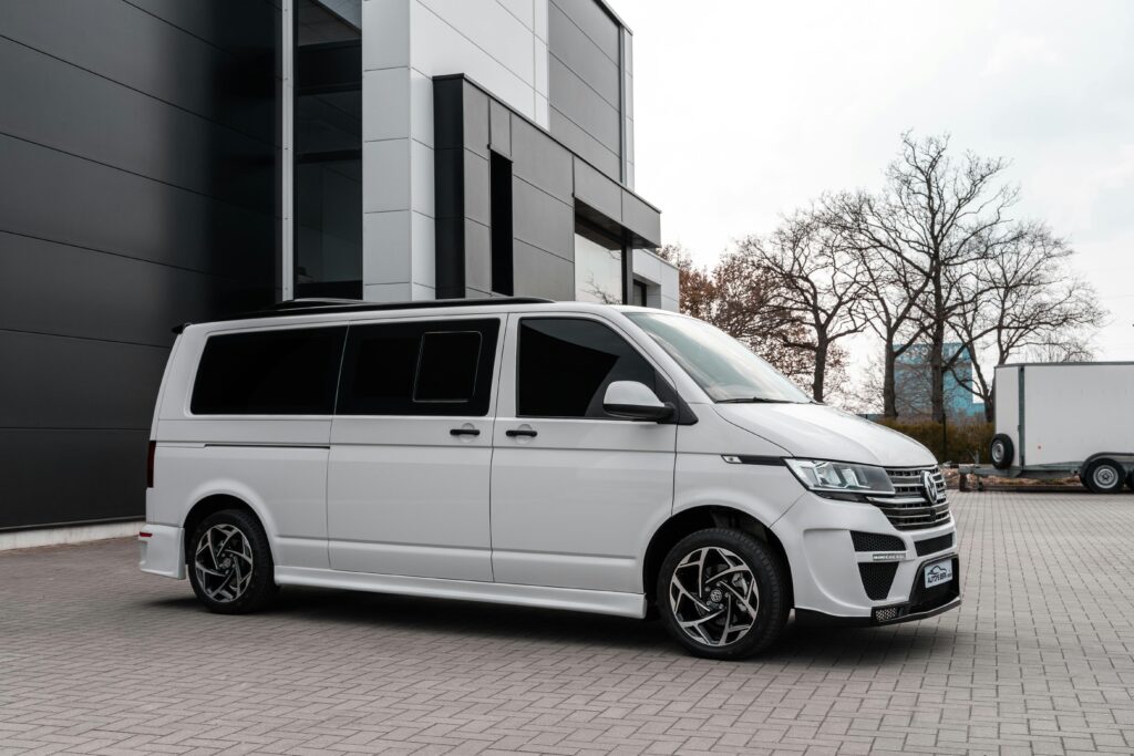 A white Volkswagen van parked beside a modern building on a paved surface.