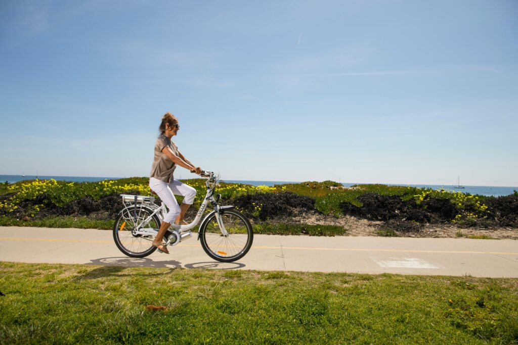 A woman enjoys a ride on an electric bike along a scenic beachside path.